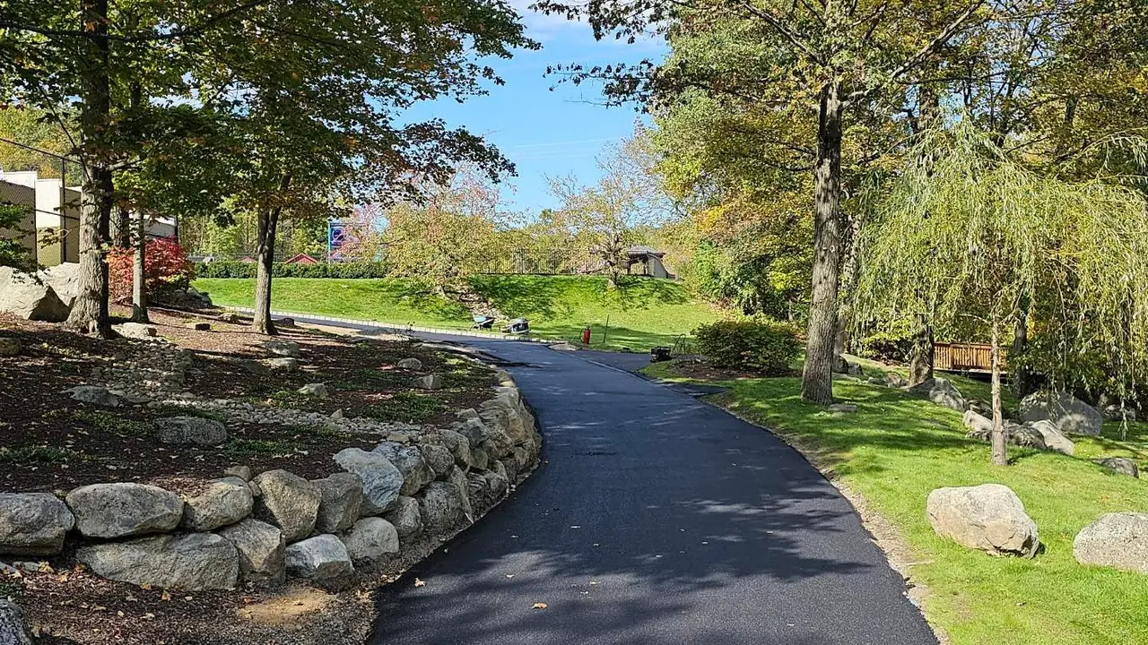 Mature asphalt driveway curving past a stone wall