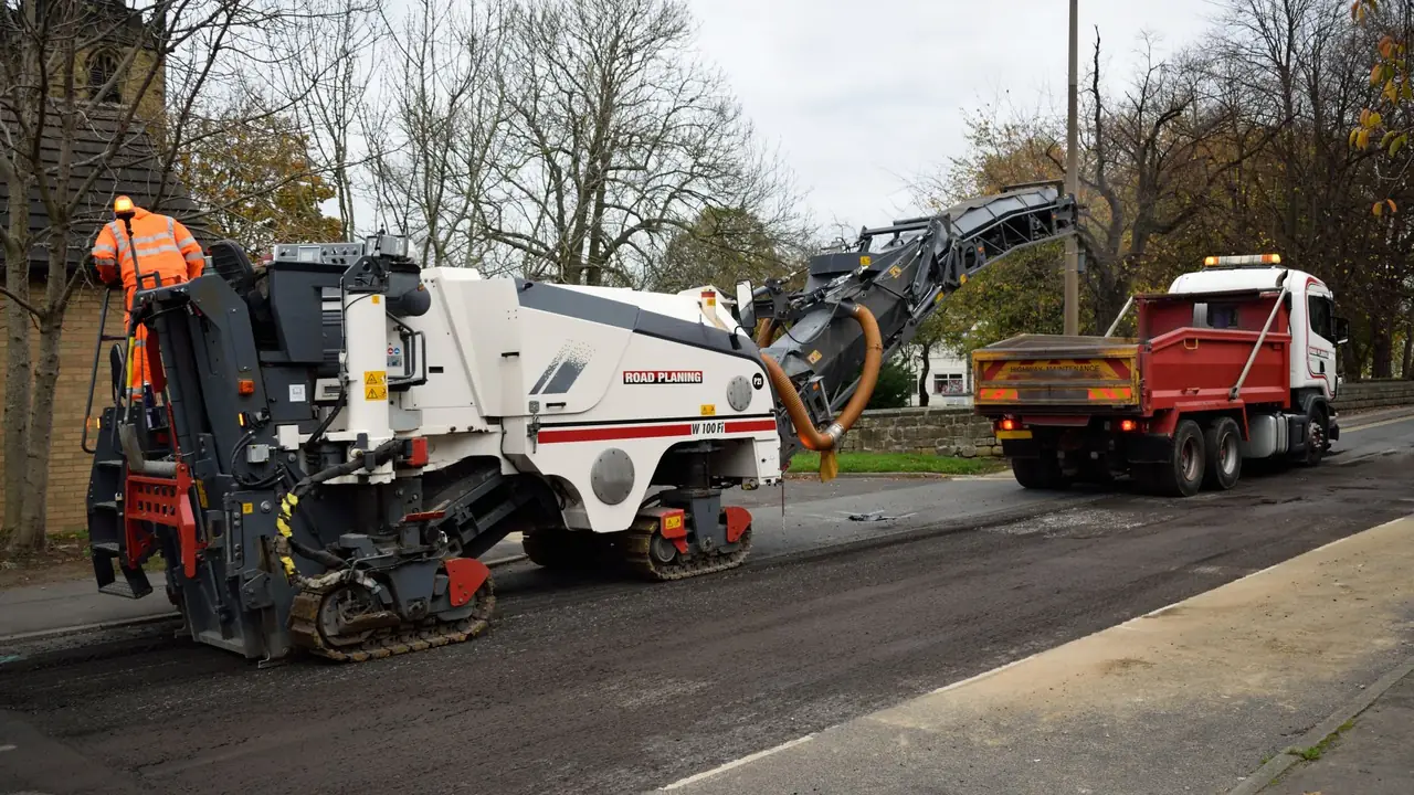 Asphalt milling machine grinding a road surface beside a haul truck