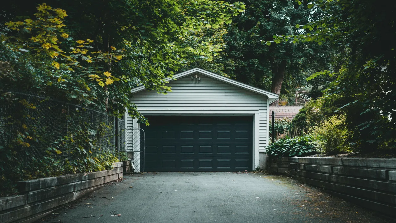 Blacktop driveway leading to a detached garage between low retaining walls and leafy trees